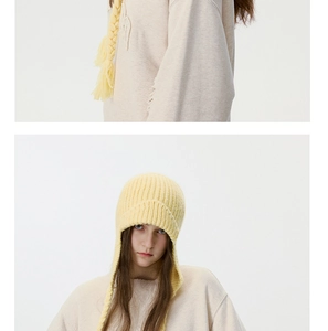 Detail of yellow ribbed knit earflap hat featuring thick braided tassels and cozy texture