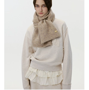 Detail of oatmeal wool scarf with metal logo tag and coarse knit texture on model