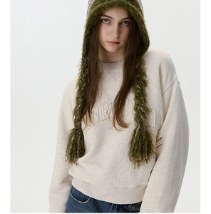 Détail du sweat crème avec broderie et chapeau en peluche verte à pampilles tressées