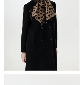 Detailed close-up of thick knitted leopard print scarf with fringe on black wool coat