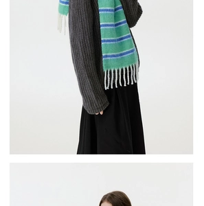 Detail of green striped wool blend scarf with white fringe tassels on model