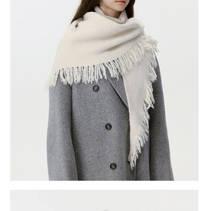 Detail of soft beige knit wool shawl with fringe tassels over a dark grey winter coat
