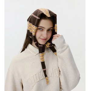 Detail of a brown and yellow striped knit headscarf with ties on a model in a beige sweater