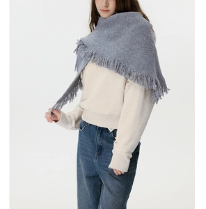 Detail of dark grey knit triangle shawl with fringe trim on soft wool blend fabric