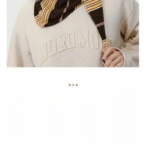 Detail of oatmeal knit sweater with MOROMO embroidered patch and striped scarf