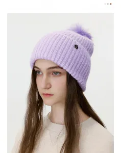 Close-up of purple knit beanie with a large pompom and circular metal logo detail