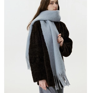 Detail of light blue wool blend scarf with fringe tassels worn over a brown coat