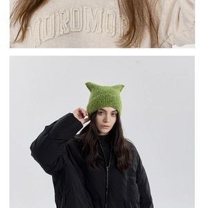 Close-up of 3D towel embroidery on beige sweatshirt and green knit cat ear beanie