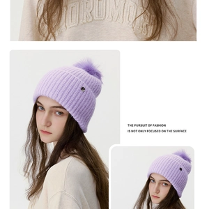 Detail of purple knitted beanie with large pompom and side circular metal logo plate