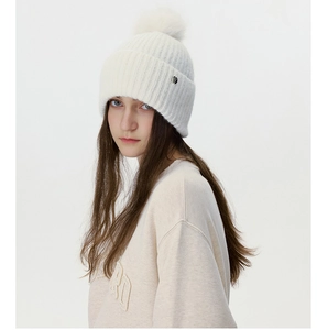 Detailed texture of white ribbed knit beanie with fluffy faux fur pom and silver charm