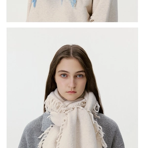 Detailed view of cream wool blend knit scarf with long tassels and embroidered accents