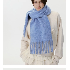 Detail of light blue knitted scarf with long fringe tassels and soft winter fabric texture