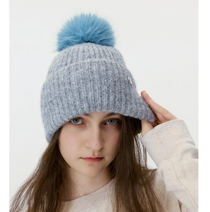 Detailed texture of grey ribbed knit hat with soft blue faux fur pompom and metal logo