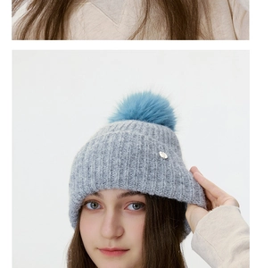 Detail of grey ribbed beanie with a vibrant blue pompom and small silver metal badge