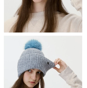 Close-up of thick grey knit texture and a fluffy blue faux fur pom-pom on the beanie