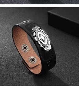 Dettaglio di un bracciale in pelle nera vintage con placca metallica a forma di sole