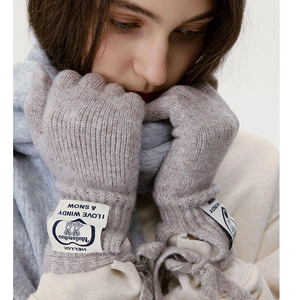 Detail von hafermehlfarbenen Strickhandschuhen mit Logo-Patch und weicher Textur