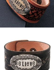 Dettaglio della piastra in metallo incisa BELIEVE su bracciale in pelle vintage goffrata
