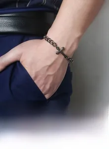 Close-up of vintage cross charm and thick Cuban link bracelet on a male wrist