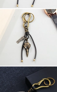 Detail view of bronze bird skull keychain with leather cord and engraved metal charm