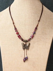 Detail of vintage ceramic bead necklace with bronze butterfly pendant and woven cord