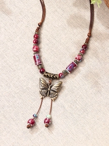 Detailed close-up of a bronze butterfly pendant with red and purple ceramic beads