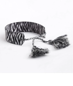 Gros plan d'un bracelet tissé motif zèbre avec des franges et glands noir et blanc