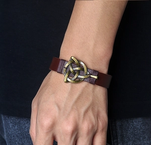 Detailaufnahme eines dunkelbraunen Lederarmbands mit bronzener keltischer Triquetra