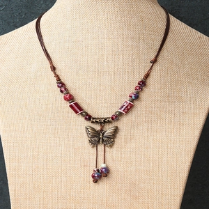 Retro butterfly ceramic pendant necklace with bronze metal wings and tassel on a beige bust