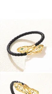 Détail du bracelet en cuir tressé avec tête de serpent dorée et yeux en pierres vertes