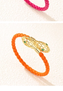 Détail du bracelet en cuir tressé avec tête de serpent dorée ajourée et yeux en gemmes vertes
