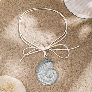 Bohemian silver conch pendant necklace with white cord bow on a sandy beach setting