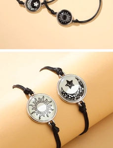 Detalle de pulseras de cuerda negra trenzada con colgantes luminosos de sol y luna