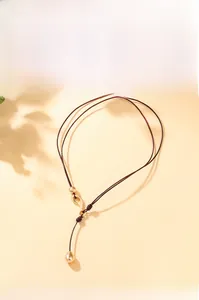 Detailed view of long brown braided cord necklace with gold metallic teardrop pendant