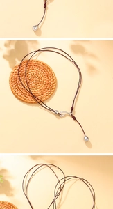 Close-up of leather cord necklace with silver teardrop pendant on natural woven background