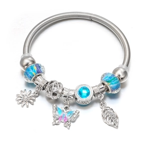 Detail of silver snake chain bracelet with blue beads, butterfly and daisy charms