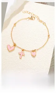 Détail du bracelet à billes dorées avec breloques cœur et croix en émail rose