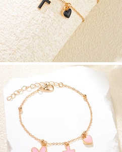 Détail de breloques cœur, croix et lettre F en émail rose et noir sur un bracelet doré
