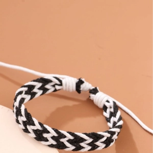 Handmade black and white woven rope bracelet with adjustable cord on red background