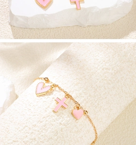 Détail d'un bracelet doré avec perles et breloques cœur et croix en émail rose