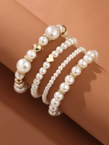 Close-up of four-piece pearl bracelet set with a gold heart pendant on a display stand