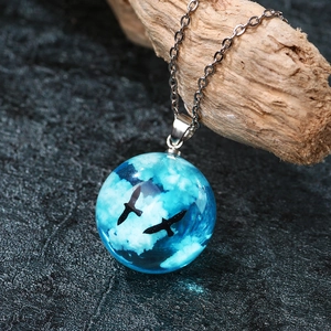 Luminous blue sky resin ball necklace featuring white clouds and bird silhouettes