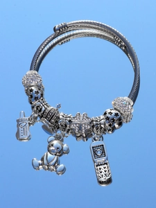 Close-up of silver beaded bracelet with teddy bear, crown, and phone charms on blue surface