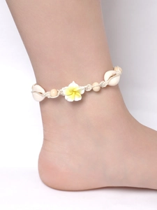 Detail of beach style woven anklet featuring shells, yellow beads and a white plumeria flower