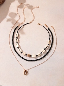 Detail of bohemian 3-piece necklace set with white shells and gold shell charms on beige