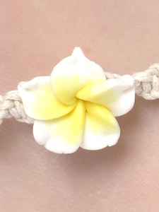 Detailed close-up of plumeria flower charm on beige hand-woven cord anklet