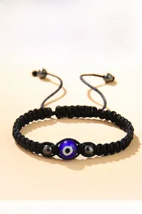 Dettaglio del bracciale in corda nera intrecciata con occhio blu e perline metalliche