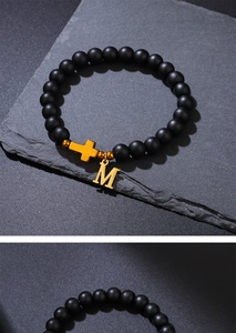 Detail of matte black agate beads with a gold cross and letter M charm on grey slate