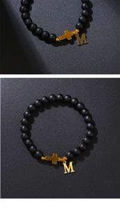 Macro shot of 8mm matte black beads with a gold cross and letter M pendant