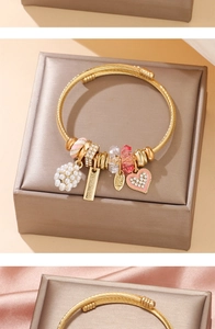 Detail of twisted gold bangle featuring white pearls, pink heart charms, and handmade tags